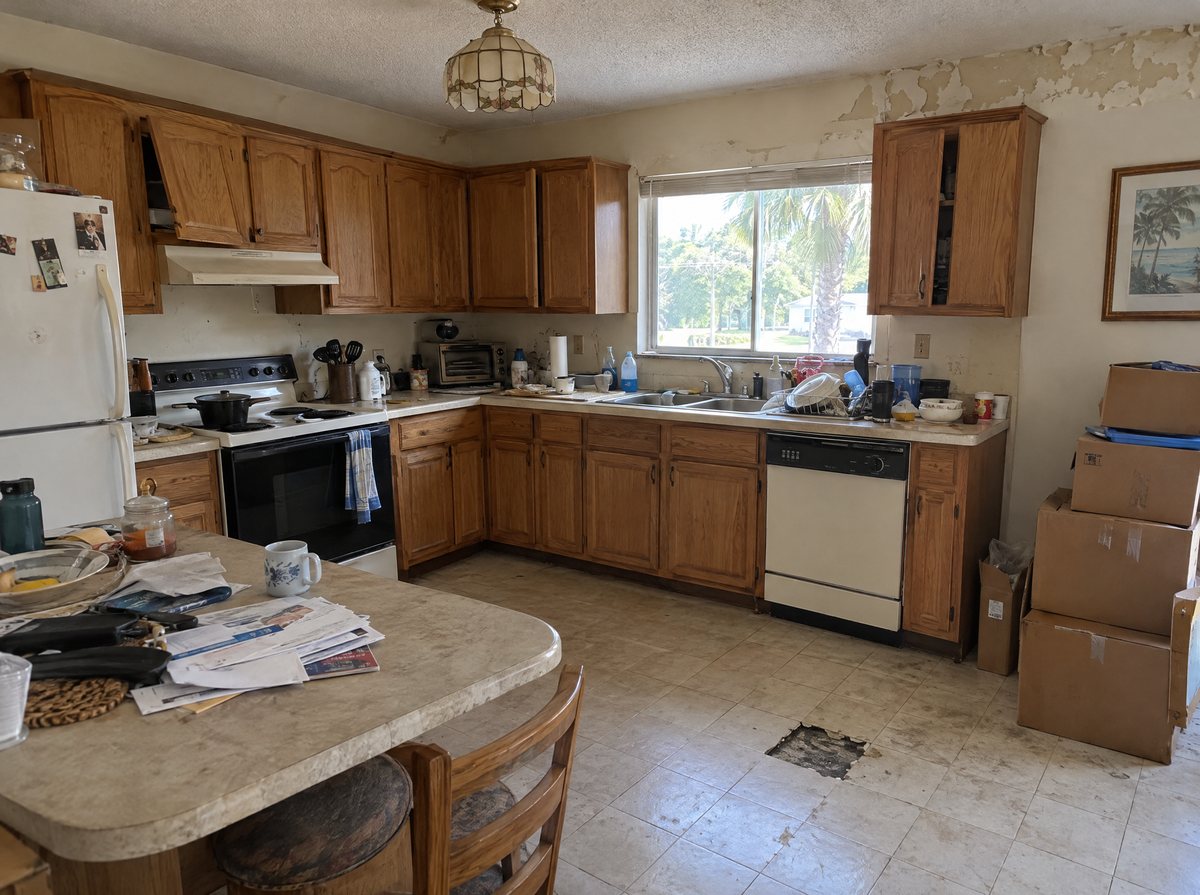 A dated, cluttered kitchen with worn cabinets and moving boxes